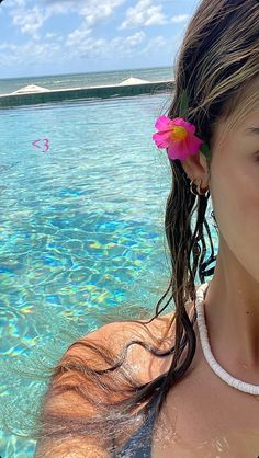 a woman standing in the water with a pink flower in her hair and wearing a white necklace