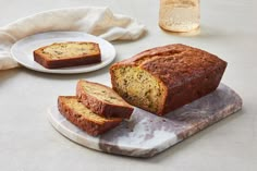 a loaf of banana bread on a marble platter next to two plates with slices