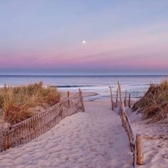 a path to the beach leading to the ocean at sunset with moon in sky above