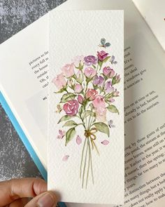 a person is holding an open book with watercolor flowers on it