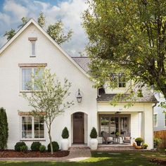 a white brick house with trees and shrubs in front of the entrance to the home