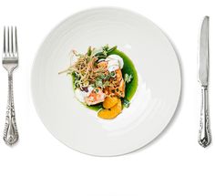 a white plate topped with shrimp and veggies next to a fork and knife