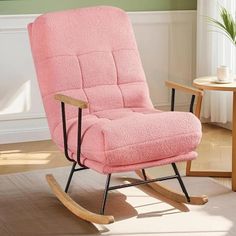 a pink rocking chair sitting on top of a hard wood floor next to a table