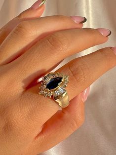 a woman's hand wearing a ring with an oval blue stone surrounded by diamonds