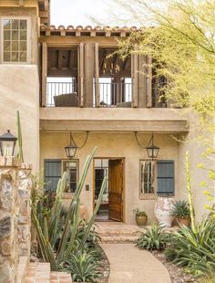 an adobe style home with cactus and succulents in front of it, surrounded by greenery