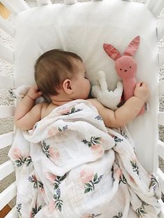 a baby sleeping in a white crib with stuffed animals on it's back