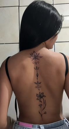 a woman with a tattoo on her back is standing in front of a tiled wall