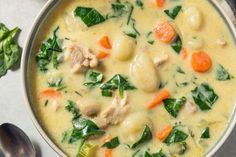 a bowl of soup with meat, spinach and carrots next to a spoon