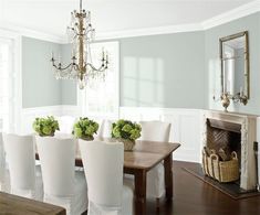 a dining room table with white chairs and green flowers in vases on the top