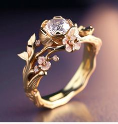 a gold ring with flowers and leaves on the side, sitting on a purple surface