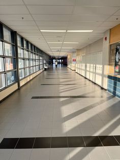 an empty hallway with lots of windows and tile flooring in the middle of it