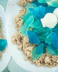 two white plates with blue and green sea glass on them next to another plate filled with sand