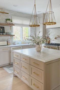 a large kitchen with white cabinets and gold hardware on the island countertop, along with two hanging lights