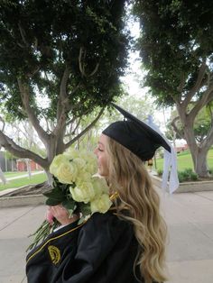 a woman in her graduation cap and gown holding flowers