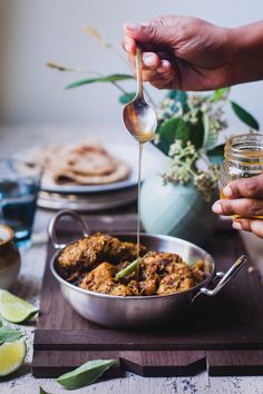 a person is spooning some food out of a pan on a wooden table with other plates and utensils