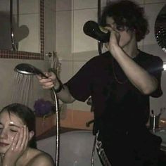 a woman is drying her hair in the shower while a man holds his hand up to his face