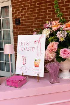 a pink table topped with lots of flowers next to a sign that says let's toast