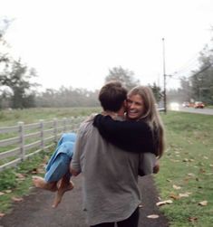 two people hugging each other while walking down a path in the grass near a fence