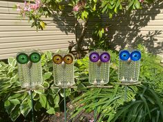 three glass owls sitting on top of metal poles in front of some bushes and flowers