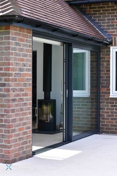 an open door to a brick building with a black stove in the corner and windows