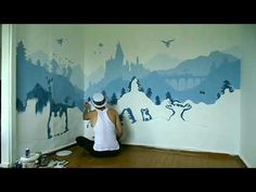 a man sitting on the floor in front of a wall painting with mountains and birds