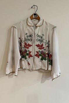 **Please note that all sales are final.** 1930's silk charmeuse bed jacket with added hand done corded flower embroidery and iridescent sequin trims. Rescued in MA in 2019, reworked in India in 2021. **Contents** * Rayon exclusive of embellishment **Care/Import** * hand wash cold, lay flat to dry * imported/vintage **Dimensions** * Neck width: 6" * Shoulder: 17" * Chest: 40" * CB Length: 20" * Sleeve Length: 18" | " Boudoir Bouquet" Bed Jacket Selected by The Falls at Free People in White, Size: Bed Jacket, Iridescent Sequin, Silk Jacket, Silk Charmeuse, Flower Embroidery, Boho Clothing, Embroidery Flowers, Boho Outfits, Lay Flat