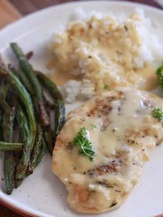 a white plate topped with meat covered in gravy and green beans