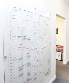 a large white board with calendars on it in an office hallway next to a doorway