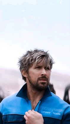 a man in a blue shirt is holding his hand up to his chest and looking off into the distance