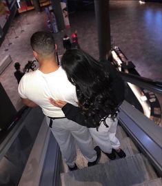 a man and woman walking down an escalator in a shopping mall, looking at each other