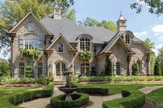 a large stone house with lots of windows and plants in the front yard, surrounded by hedges