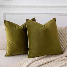 two green pillows sitting on top of a couch next to a white pillow case and blanket