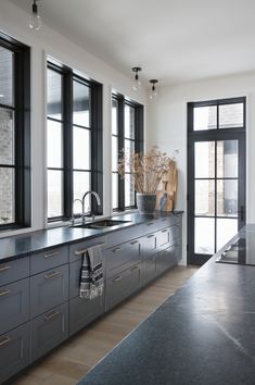 a kitchen with black counter tops and wooden flooring next to large windowed windows