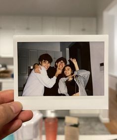 a person holding up a polaroid with two people taking a photo together in the kitchen