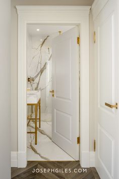 an open door leading to a bathroom with marble floors and walls, along with a gold bar stool