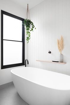 a white bath tub sitting under a window next to a shelf with plants on it