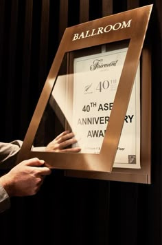 a person holding up a framed poster in front of a black curtain with the words ballroom on it