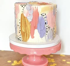 a multicolored cake sitting on top of a pink stand next to a white wall