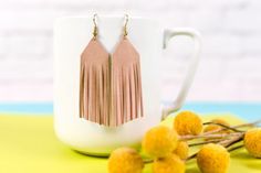 a pair of pink tasselled earrings sitting on top of a white cup next to berries