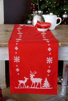 a red table cloth with white reindeers and snowflakes on it in front of a christmas tree