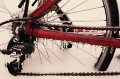 a red bike with icicles on the front wheel and rear tire is parked in the snow