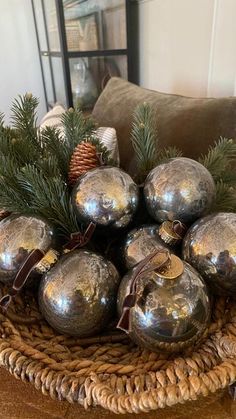 a basket filled with lots of shiny silver balls on top of a wooden table next to a christmas tree