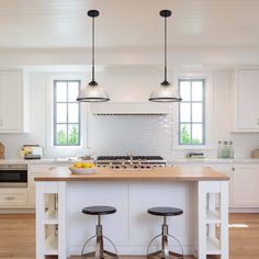 two stools sit at the center of a kitchen island with three lights hanging over it