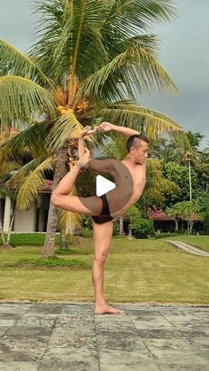 a man standing on one leg in front of a palm tree and doing a handstand