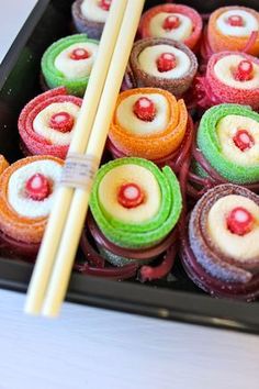 there are many colorful cupcakes with chopsticks in the tray on the table