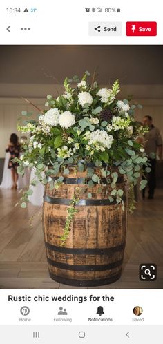 a wooden barrel filled with white flowers and greenery on top of a hard wood floor