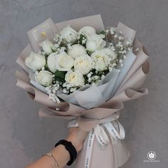 a bouquet of white roses is being held by a woman's hand on a gray background