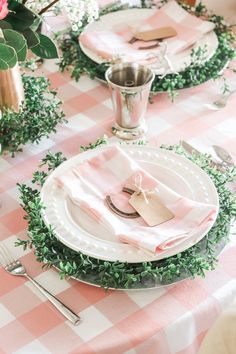 the table is set with pink and white checkered linens, silverware, and greenery