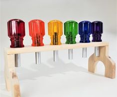 a wooden bench with six different colored glass vases sitting on it's legs