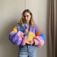 a woman standing in front of a window wearing a multicolored sweater and jeans